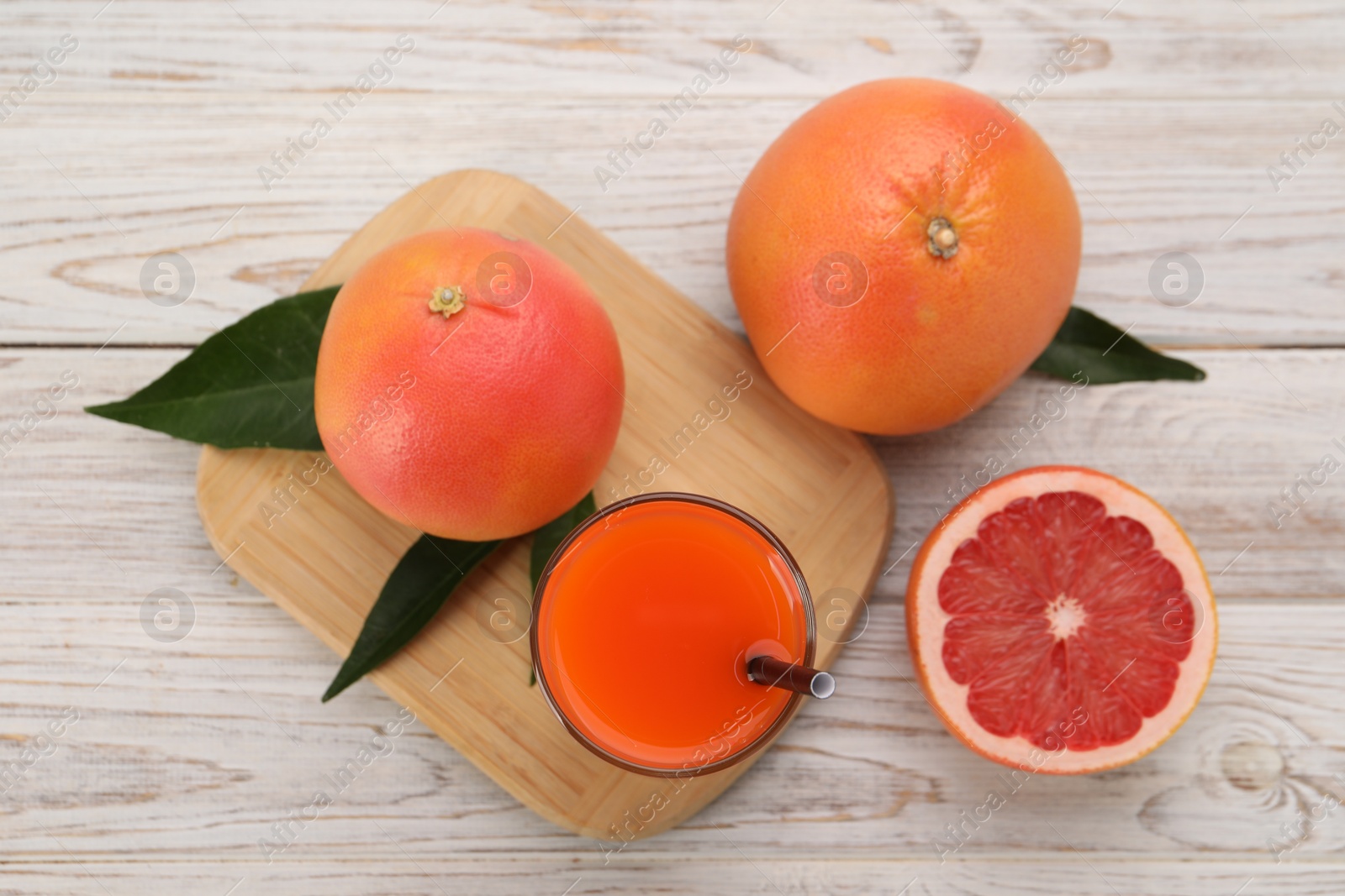 Photo of Tasty grapefruit juice in glass and fresh fruits on light wooden table, flat lay