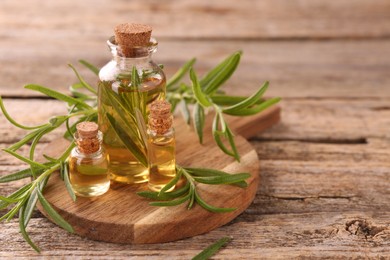 Photo of Aromatic essential oils in bottles and rosemary on wooden table, closeup. Space for text