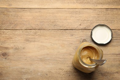 Photo of Spicy mustard in glass jar on wooden table, above view. Space for text