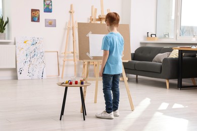 Photo of Little boy painting in studio, back view. Using easel to hold canvas