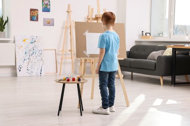 Little boy painting in studio, back view. Using easel to hold canvas