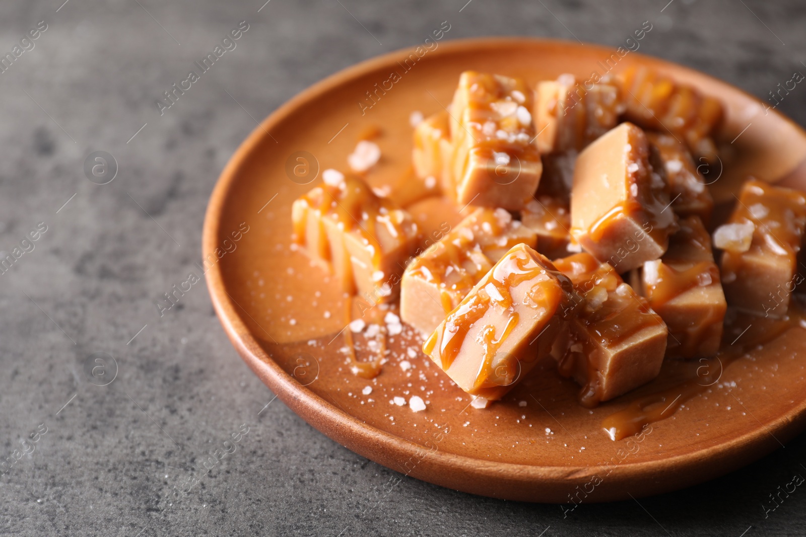 Photo of Plate with tasty candies, caramel sauce and salt on grey table, closeup