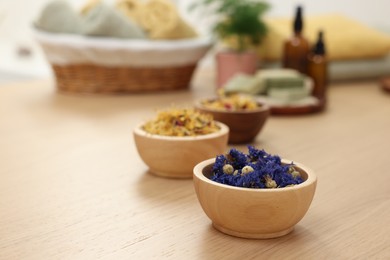 Bowls of dry flowers on light wooden table, space for text. Spa therapy