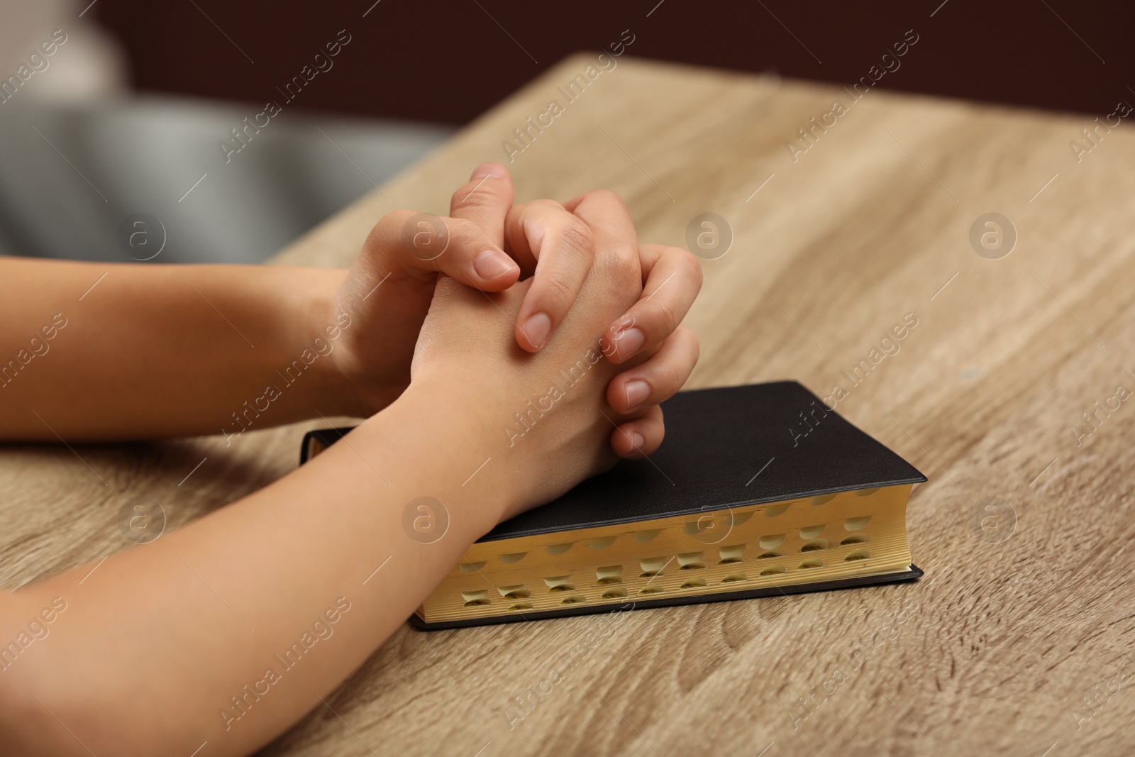 Photo of Religious woman praying over Bible at wooden table indoors, closeup