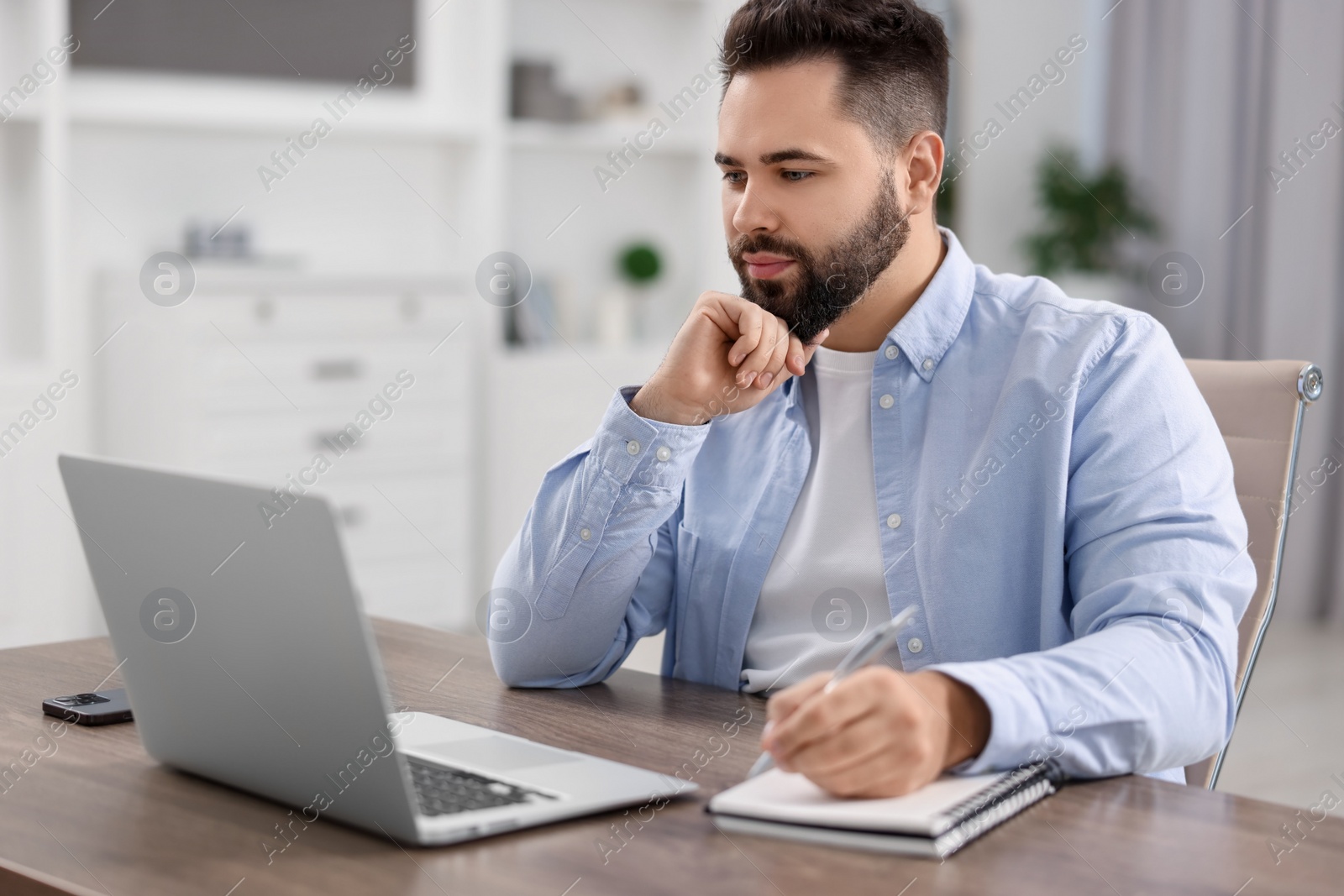 Photo of Young man watching webinar at table in room