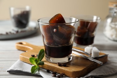 Photo of Glass of coffee with ice cubes, mint and sugar on white wooden table, closeup