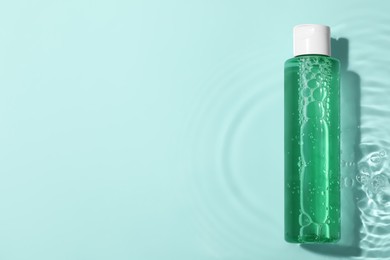 Photo of Wet bottle of micellar water and petals on light blue background, top view. Space for text