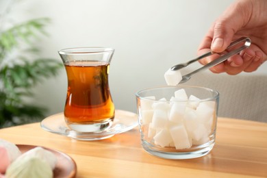 Woman adding sugar cube into aromatic tea at wooden table indoors, closeup