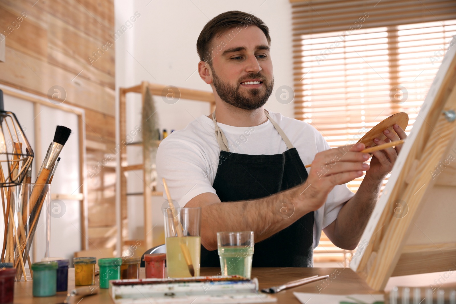 Photo of Young man painting on easel with brush in artist studio