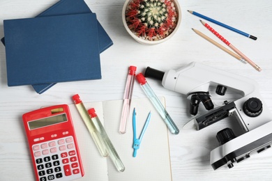 Photo of Laboratory glassware, microscope and school supplies on wooden background, flat lay