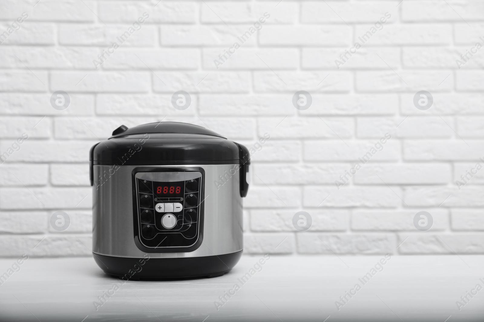 Photo of Modern electric multi cooker on table near brick wall. Space for text