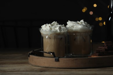 Photo of Glasses of iced coffee and chocolate on wooden table against blurred lights, closeup. Space for text