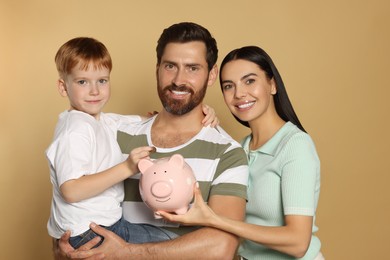 Photo of Happy family with ceramic piggy bank on beige background
