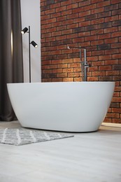 Photo of Stylish bathroom interior with ceramic tub near brick wall