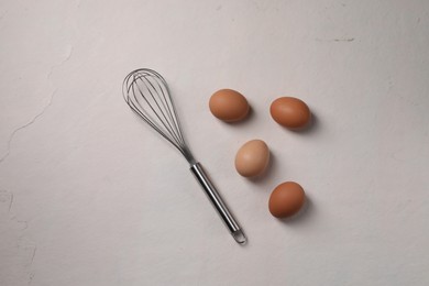 Photo of Metal whisk and raw eggs on light table, flat lay