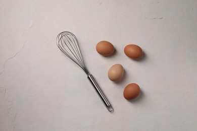 Metal whisk and raw eggs on light table, flat lay