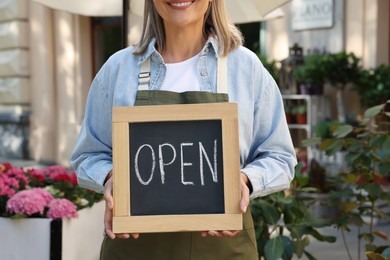 Photo of Business owner holding open sign near her flower shop outdoors, closeup