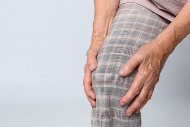 Senior woman having knee problems on grey background, closeup. Space for text