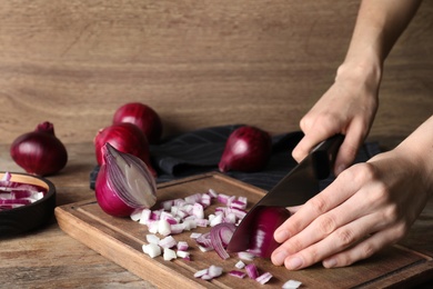 Photo of Young woman cutting ripe red onion on board at wooden table, closeup