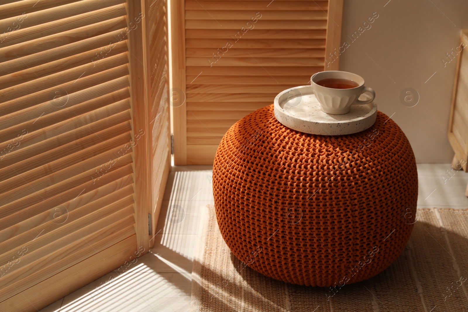 Photo of Tray with cup of tea on stylish comfortable pouf in room. Home design