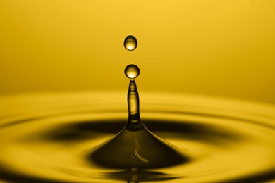 Splash of golden oily liquid with drop on yellow background, closeup