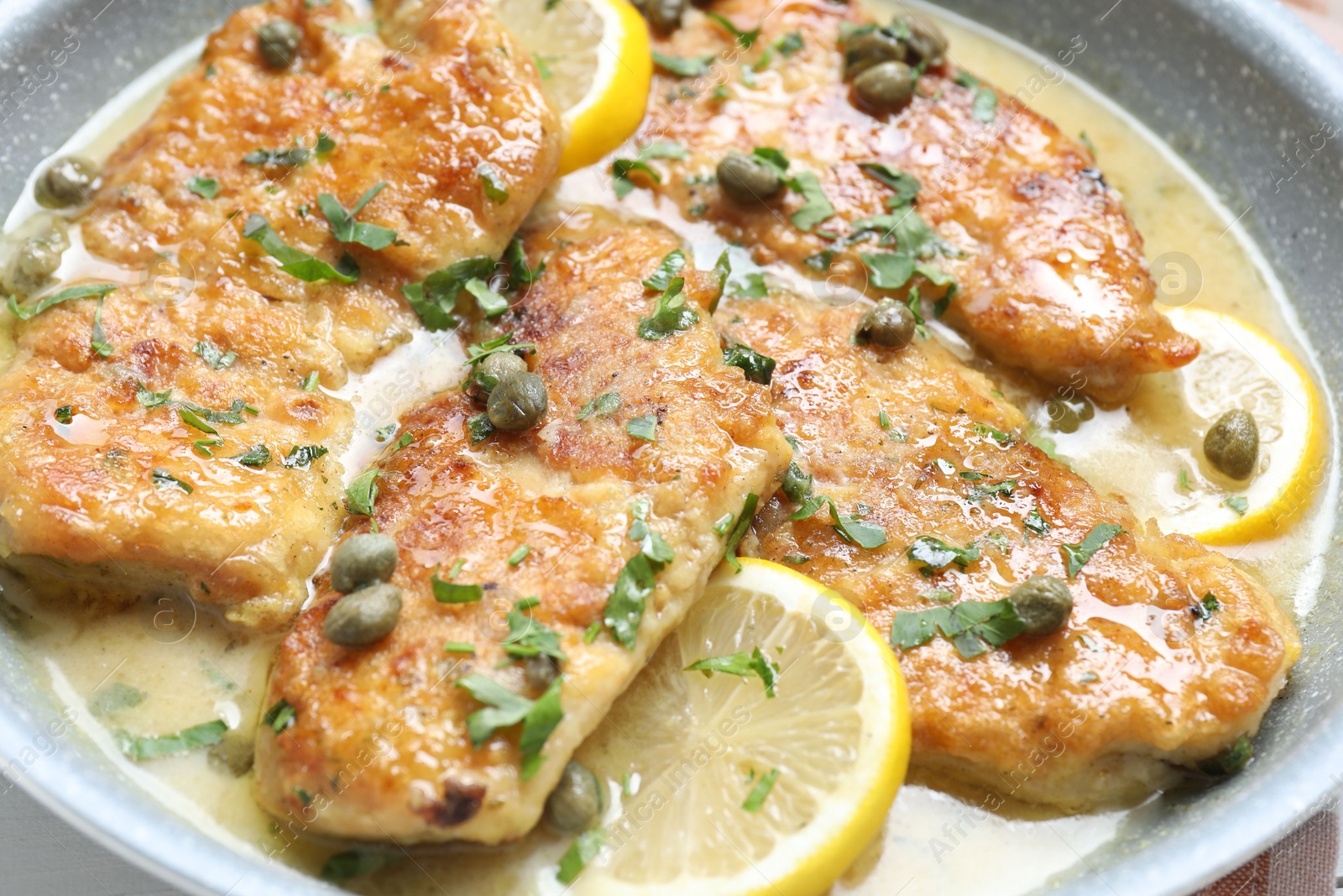 Photo of Delicious chicken piccata with lemons and herbs in pan, closeup