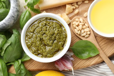 Photo of Tasty pesto sauce in bowl, basil, pine nuts, garlic, oil and cheese on table, top view