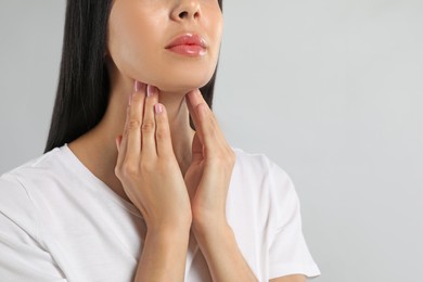 Photo of Young woman doing thyroid self examination on light background, closeup