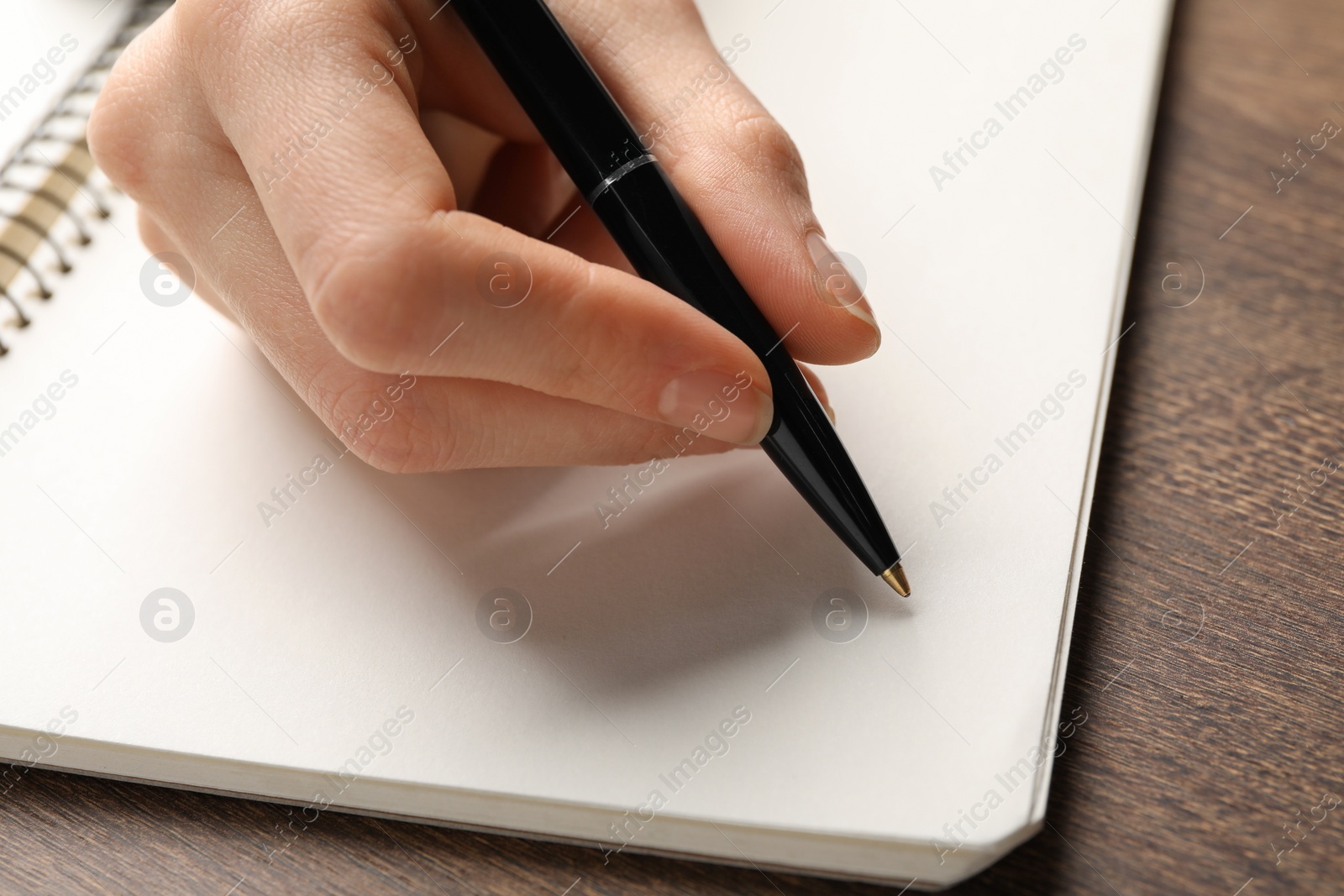 Photo of Woman writing in notebook at wooden table, closeup