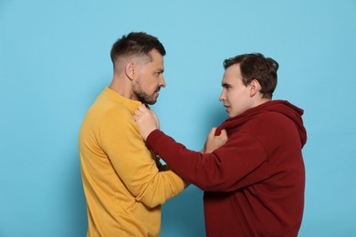 Photo of Two emotional men fighting on light blue background