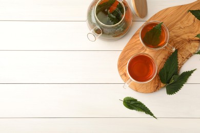 Photo of Aromatic nettle tea and green leaves on white wooden table, flat lay. Space for text