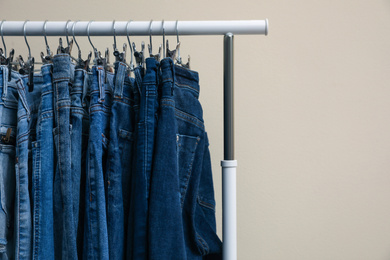 Rack with stylish jeans on color background, closeup