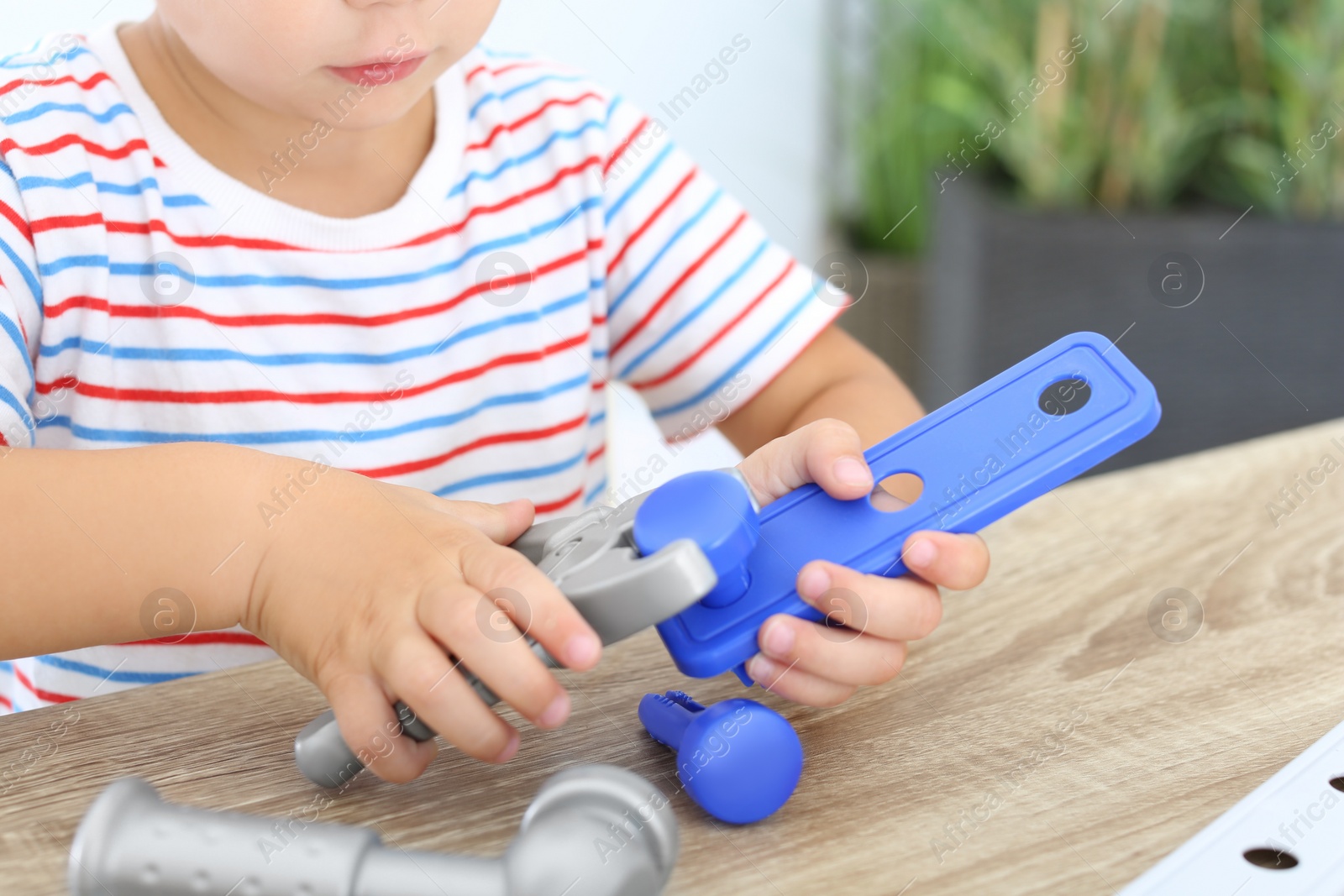 Photo of Little boy playing with toy construction tools at wooden table, closeup