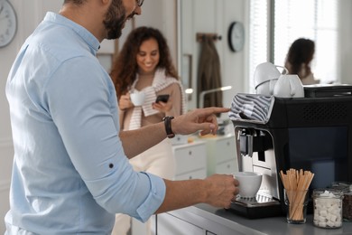 Photo of Man talking with colleague while using modern coffee machine in office, closeup
