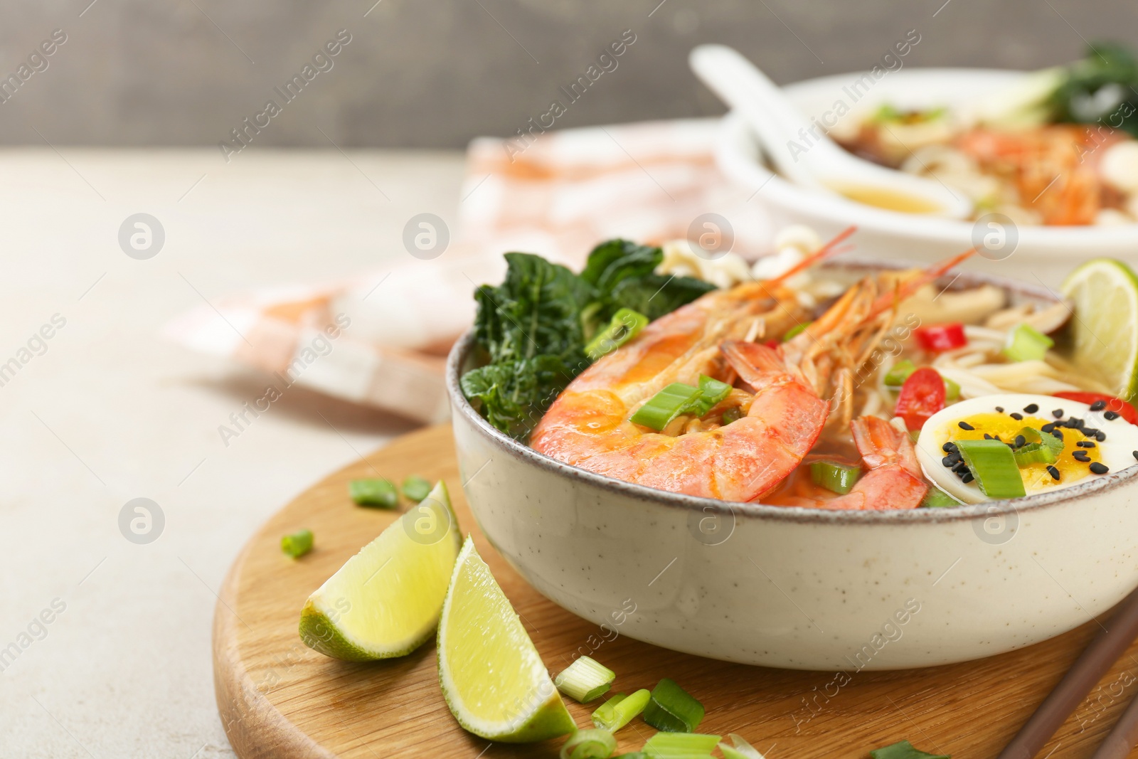 Photo of Delicious ramen with shrimps and egg in bowl on light textured table, space for text. Noodle soup