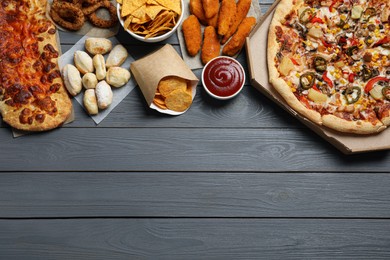 Pizza, chips and other fast food on gray wooden table, flat lay with space for text