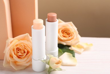 Photo of Stylish presentation of different lip balms with rose flowers on white table, space for text
