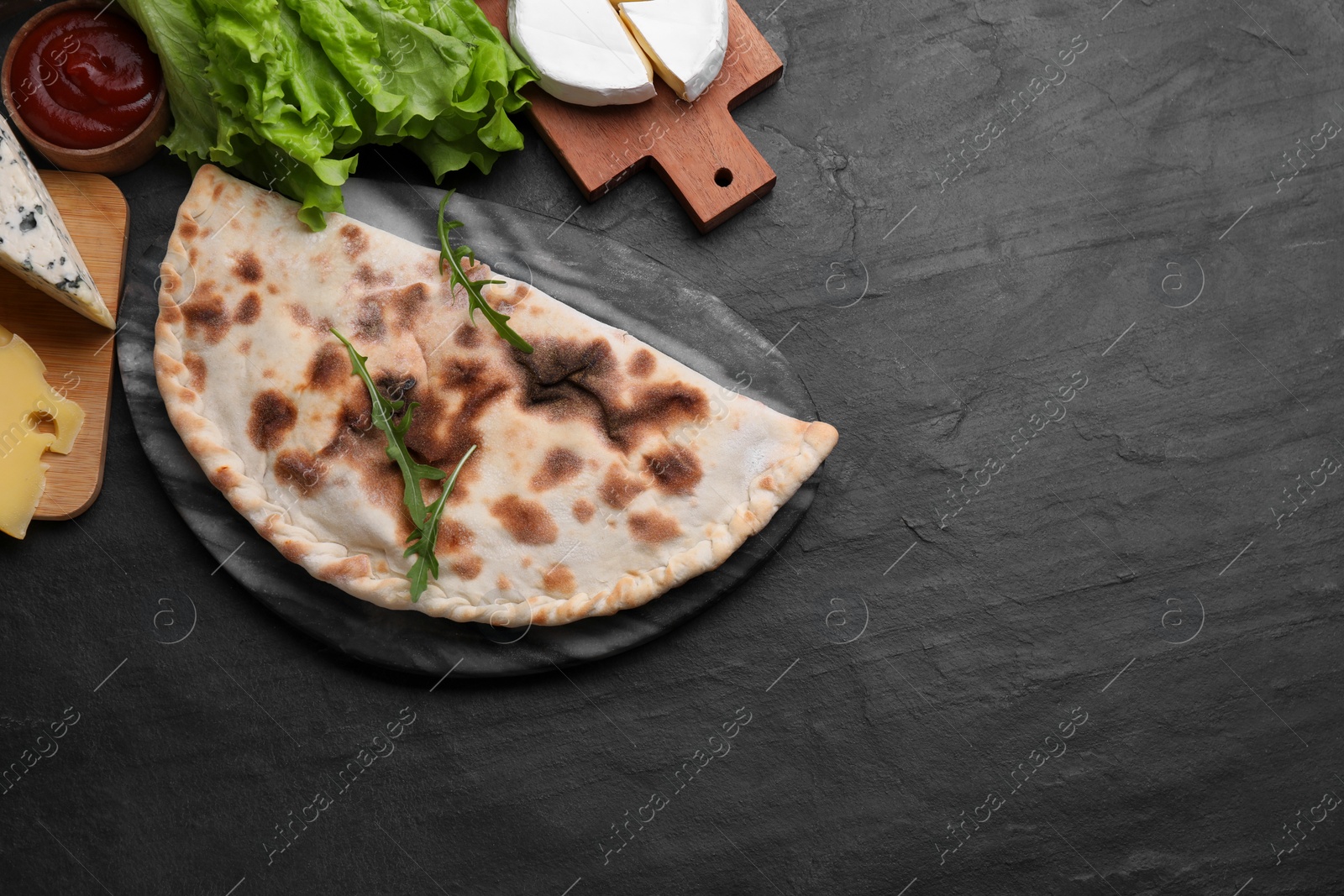 Photo of Delicious calzone and products on black table, flat lay. Space for text