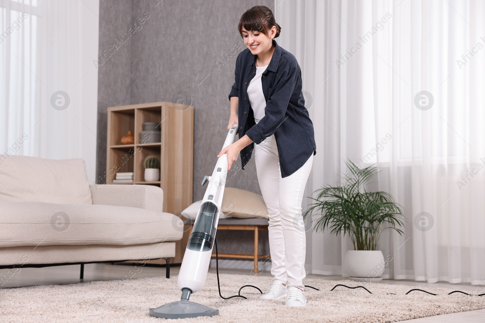 Photo of Happy young housewife vacuuming carpet at home