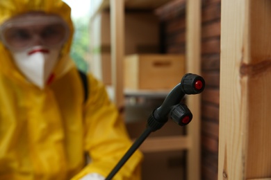 Pest control worker spraying pesticide indoors, focus on nozzle