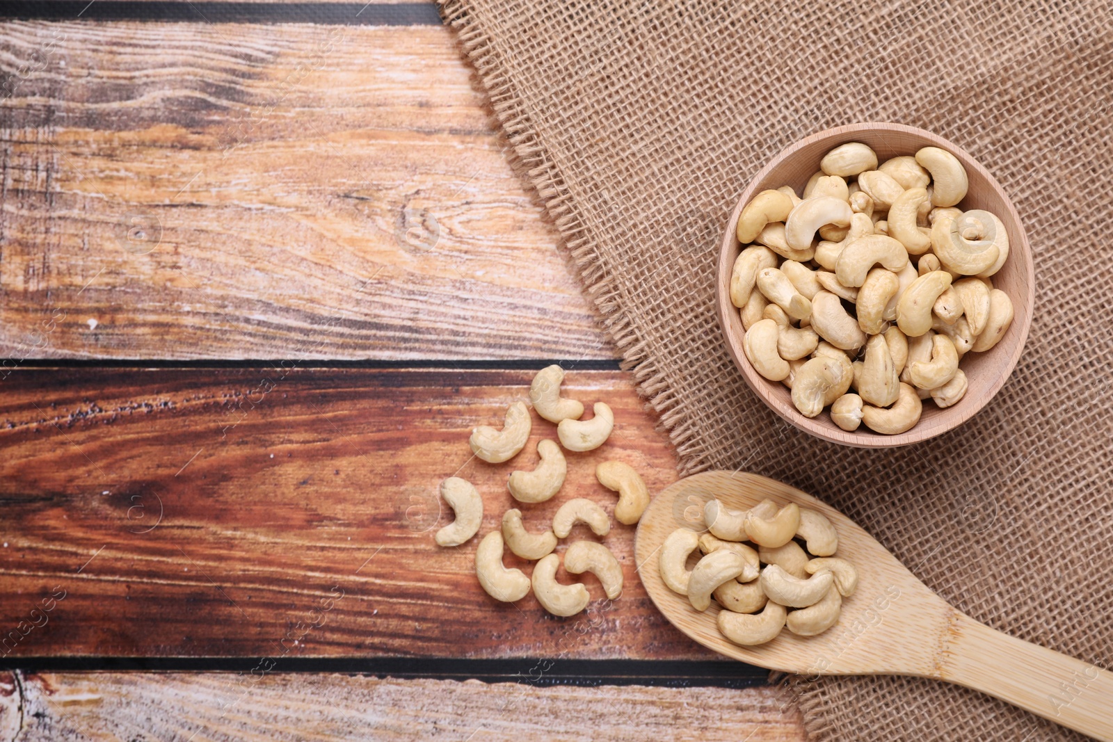 Photo of Tasty cashew nuts in bowl and spoon on wooden table, flat lay. Space for text