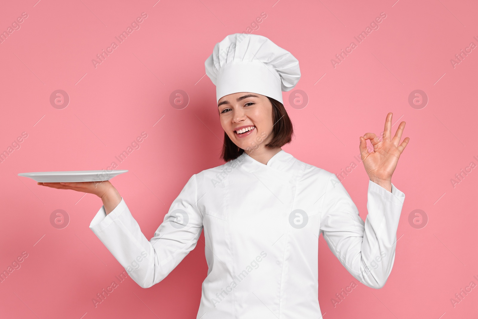 Photo of Happy confectioner with plate showing ok gesture on pink background