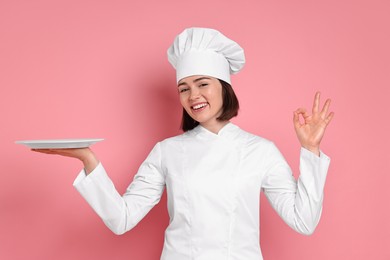 Photo of Happy confectioner with plate showing ok gesture on pink background