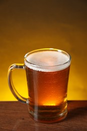 Mug with fresh beer on wooden table against dark background