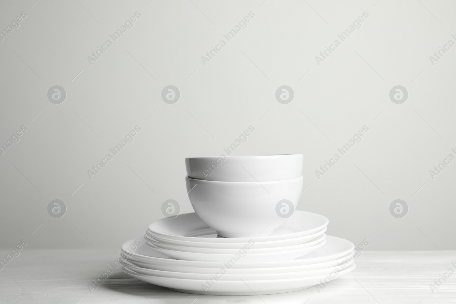 Photo of Stack of clean plates and bowls on wooden table against white background. Space for text