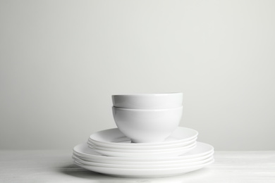 Stack of clean plates and bowls on wooden table against white background. Space for text