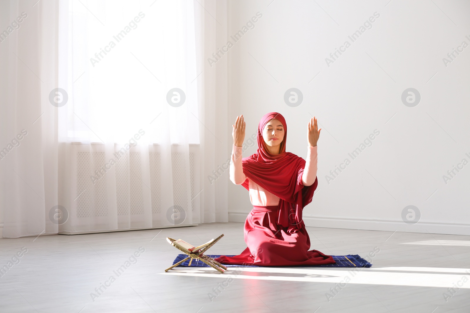 Photo of Muslim woman in hijab praying on mat indoors