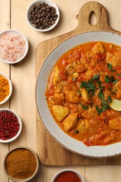 Photo of Delicious chicken curry and spices on wooden table, flat lay