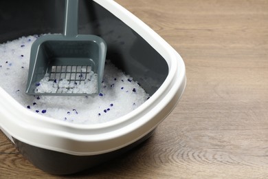 Cat litter tray with filler and scoop on wooden floor, closeup. Space for text
