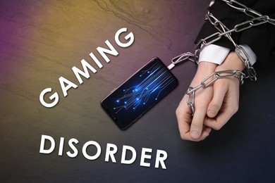 Image of Gaming disorder. Man showing chained hands to smartphone at table, top view. Circuit board pattern on device screen